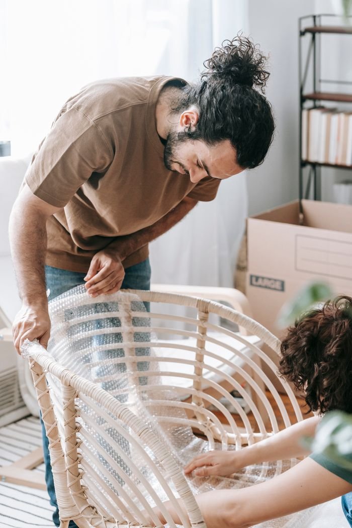 Couple wrapping a chair with bubble wrap during relocation in a bright room.